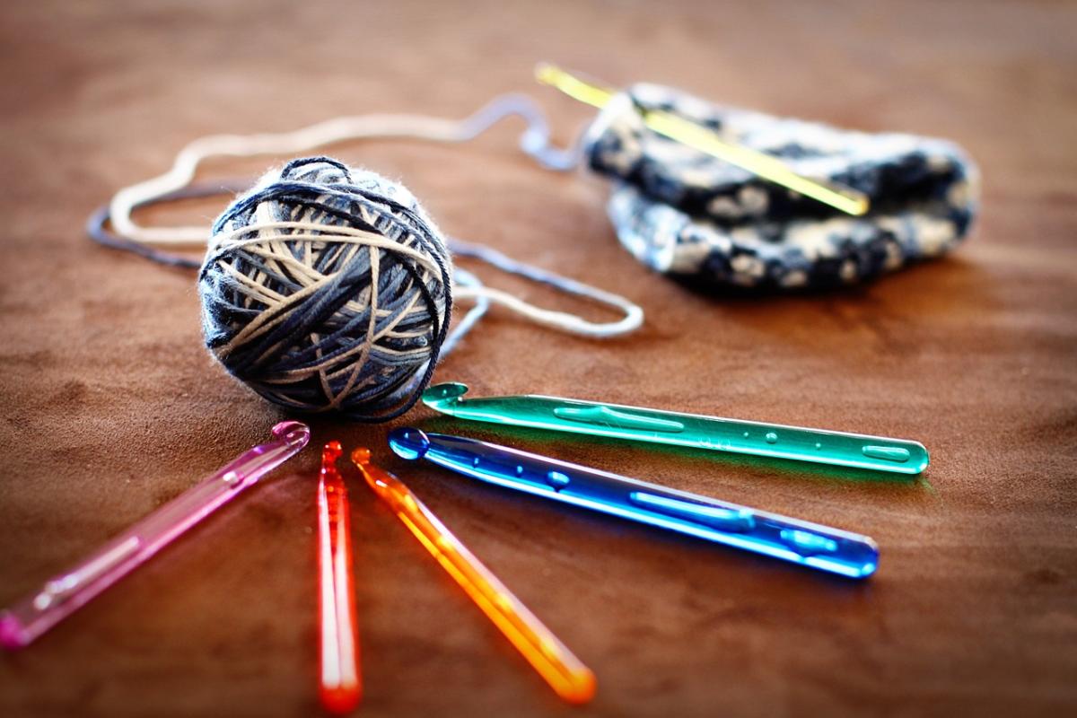 Ball of blue and white yarn with brightly colored crochet hooks and project in the background